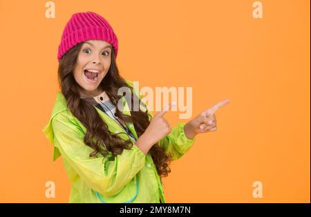 Choisissez entre le plus mignon et le plus tendance. Fille cheveux longs fond jaune. Concept de saison froide. Accessoire mode hiver. Petit enfant portant un chapeau chaud Banque D'Images