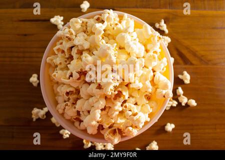 Goiania, Goias, Brésil – 04 février 2023 : un bol rempli de pop-corn, avec un peu de pop-corn répandu sur la table en bois. Banque D'Images