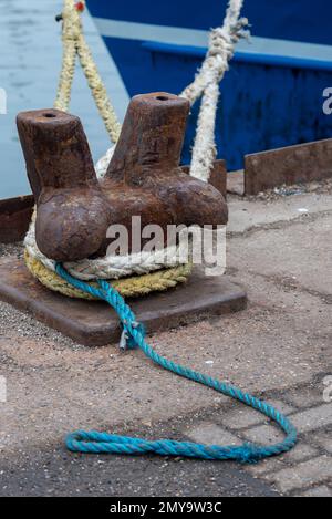 Vieux bollard d'amarrage en métal rouillé avec des couleurs différentes roppé attaché autour d'elle au quai de carrossage, Portsmouth, Angleterre. Banque D'Images