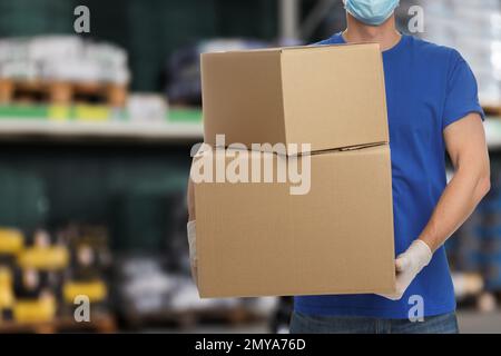 Homme portant un uniforme et un masque médical avec des boîtes en carton en magasin, fermer. Marché de gros Banque D'Images