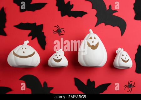 Porte-bougie en forme de citrouille blanche avec chauves-souris décoratives et araignées sur fond rouge, pose plate. Fête d'Halloween Banque D'Images