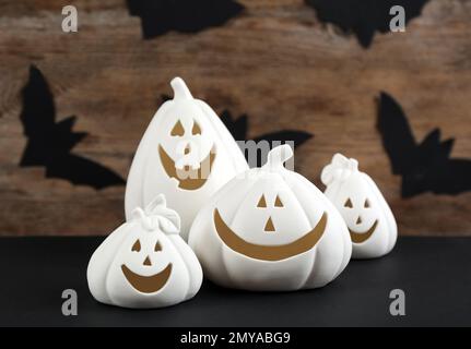 Porte-bougie en forme de citrouille blanche sur une table noire contre un mur en bois avec des chauves-souris en papier. Décoration d'Halloween Banque D'Images