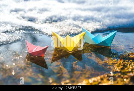 Bateaux en papier multicolores. Coloré rose jaune bleu orange navires dans la grande pouffle de neige de printemps sur la rue d'hiver. Temps chaud humide pluvieux, herbe ancienne. Bonjour Banque D'Images