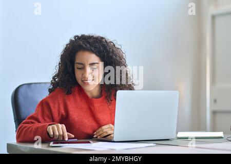 Jeune femme d'affaires latine souriante assise au bureau à l'aide d'une tablette numérique. Banque D'Images