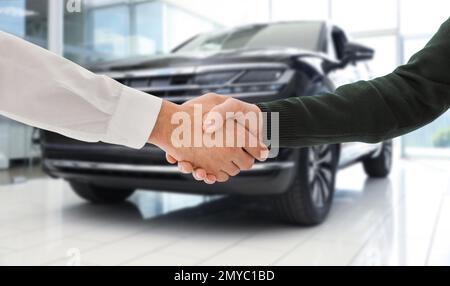 Homme achetant la voiture et en serrant la main avec le vendeur contre l'auto floue, gros plan Banque D'Images