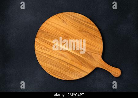 Table de service ronde en bois vide avec poignée sur fond de béton noir ancien, table en sorbde. Vue de dessus. Modèle de nourriture, espace de copie. Pose à plat Banque D'Images