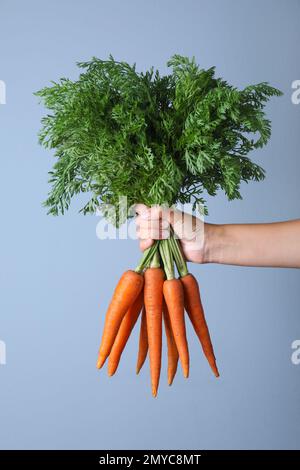 Femme tenant des carottes mûres sur fond bleu clair, gros plan Banque D'Images