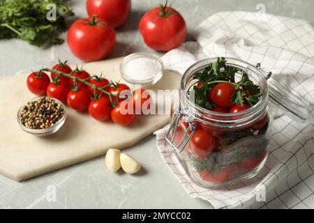 Pot de pickling avec tomates cerises mûres fraîches et épices sur table grise Banque D'Images