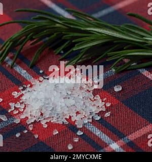 pile de gros sel de mer et une branche de romarin sur une nappe rouge Banque D'Images