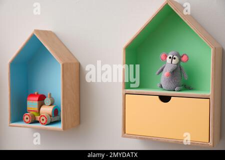 Étagères élégantes en forme de maison avec jouets sur un mur blanc. Décoration intérieure de la chambre de bébé Banque D'Images