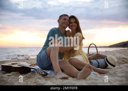 Couple charmant ayant un pique-nique romantique sur la plage au coucher du soleil Banque D'Images