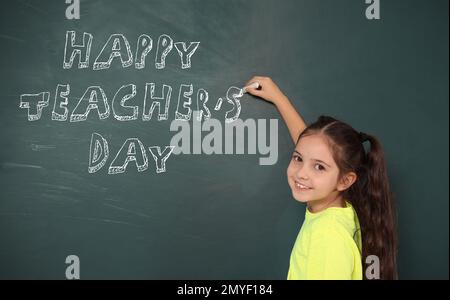 Jolie petite fille écrivant l'expression Happy Teacher's Day sur le tableau noir Banque D'Images