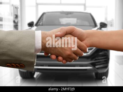 Homme achetant la voiture et en serrant la main avec le vendeur contre l'auto floue, gros plan Banque D'Images