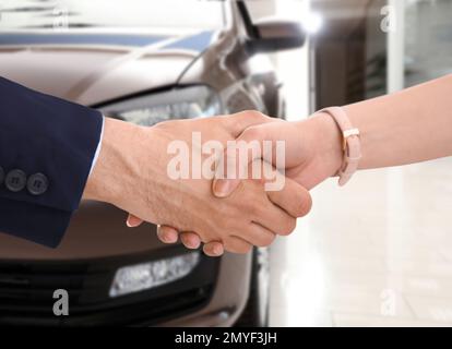 Femme achetant la voiture et se serrer les mains avec le vendeur contre l'auto floue, gros plan Banque D'Images