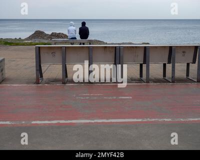 Un couple est assis sur un banc au bord de la mer. Temps nuageux à la station. Pas la saison du tourisme. Loisirs sur la côte. Remblai de Banque D'Images