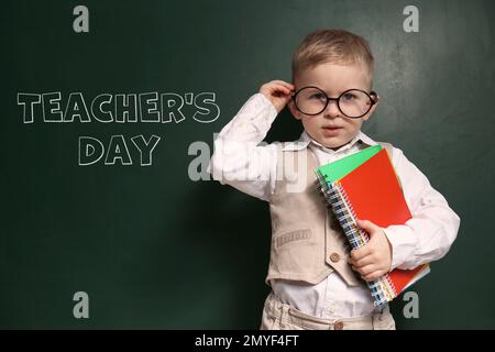 Mignon petit enfant portant des lunettes près du tableau noir avec texte Journée de l'enseignant Banque D'Images