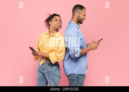 Curieuse femme noire essayant de regarder le smartphone de son petit ami, gars utilisant le gadget et de discuter, se tenant dos à dos Banque D'Images