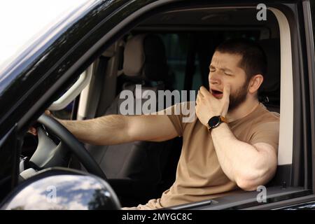 Un homme fatigué bâilling en conduisant sa voiture moderne Banque D'Images