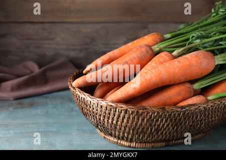 Carottes fraîches dans un panier sur une table en bois bleu, gros plan Banque D'Images