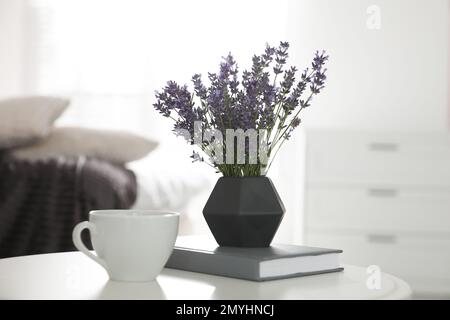 Belles fleurs de lavande, tasse de café et livre sur table blanche à l'intérieur Banque D'Images