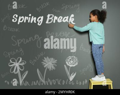 African American girl écrivant phrase Spring Break avec craie sur le mur gris. Vacances scolaires Banque D'Images