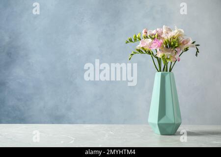 Superbes freesias en fleurs dans un vase sur une table sur fond bleu. Espace pour le texte Banque D'Images