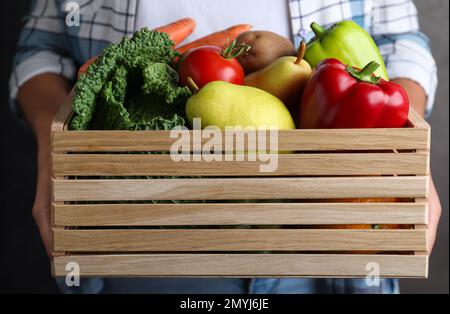 Fermier tenant une caisse en bois remplie de légumes frais et de fruits sur fond gris, gros plan Banque D'Images