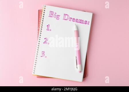 Carnet avec liste de rêves et stylo sur table rose, vue du dessus Banque D'Images