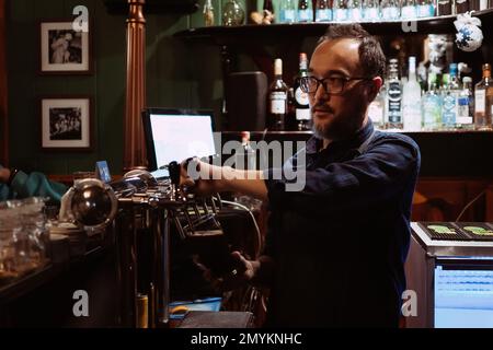 le barman au bar verse de la bière dans un verre avec un robinet d'un fût Banque D'Images