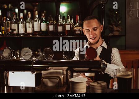 le barman verse de la bière à la pression dans un verre depuis le robinet situé derrière le comptoir du bar dans le pub Banque D'Images