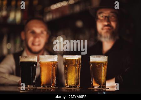 quatre verres avec différentes bières sur le comptoir du bar dans le pub sur fond de barmen Banque D'Images