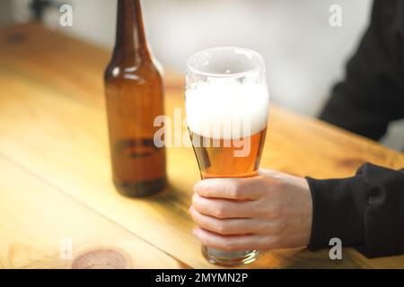 personne tenant une tasse à bière près d'une bouteille sur une table en bois Banque D'Images