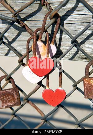Serrures d'amour rouges en forme de coeur sur une clôture au bord de l'océan. Banque D'Images