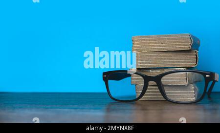 Pile de livres avec des lunettes sur fond bleu et espace de copie. Banque D'Images