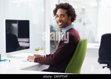 Il aime vraiment son travail. un jeune homme d'affaires assis à un bureau. Banque D'Images