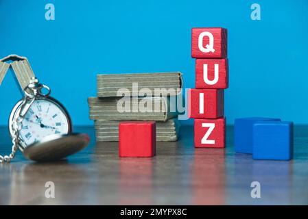 Une montre de poche, une pile de livres et un cube en bois rouge écrit avec UN QUIZ sur une table. Banque D'Images
