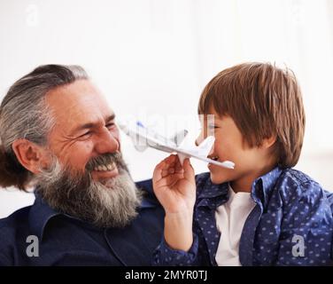 Ils partagent un amour pour l'avion. un jeune garçon assis sur ses grands-pères en toile jouant avec un jouet jet. Banque D'Images