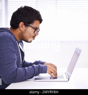 Obtenir son diplôme par correspondance. un beau jeune homme qui travaille sur son ordinateur portable dans un bureau. Banque D'Images