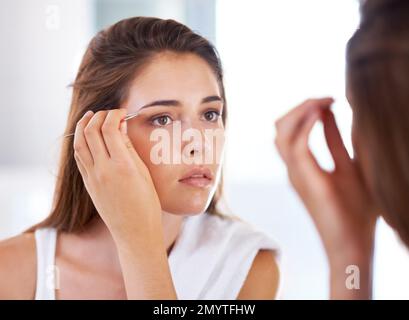 Les façonner à la perfection. Une jeune femme en train de touiller ses sourcils devant un miroir. Banque D'Images