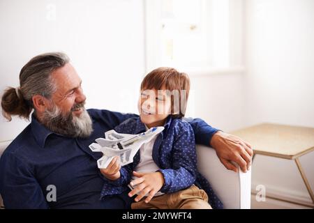 Montrant à grand-père son nouveau jet. un jeune garçon assis sur ses grands-pères en toile jouant avec un jouet jet. Banque D'Images