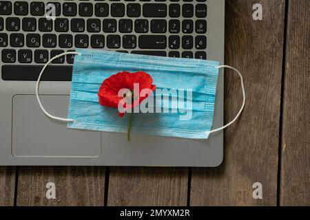 un masque médical se trouve sur un ordinateur portable et une fleur de pavot sur une table Banque D'Images