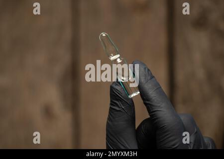 la main dans les gants tient une ampoule avec le médicament Banque D'Images