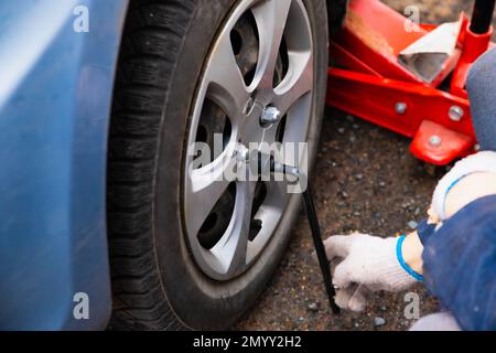 Changement de roue, la voiture est soulevée à l'aide d'un cric. Les mains mâles dévisse les rondelles de roue à l'aide d'une clé à bille. Banque D'Images