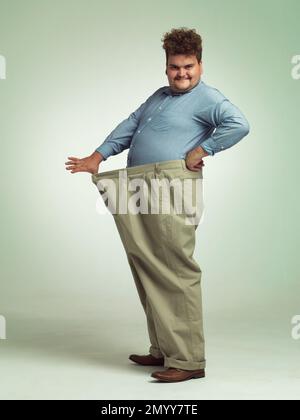 Mon régime va bien. un homme en surpoids portant une paire de pantalons surdimensionnés qui a l'air heureux. Banque D'Images
