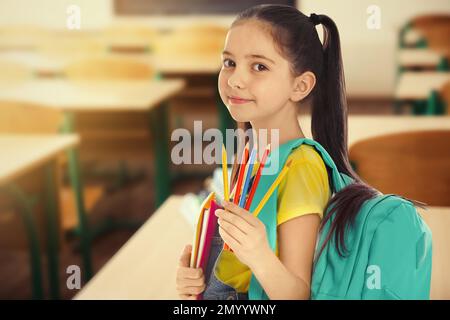 Petite fille avec papeterie d'école dans la salle de classe vide Banque D'Images