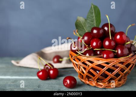 Cerises sucrées juteuses avec des feuilles sur une table en bois sur fond bleu, gros plan. Espace pour le texte Banque D'Images