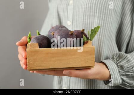 Femme tenant une caisse en bois avec de savoureuses figues crues sur fond gris clair, gros plan Banque D'Images