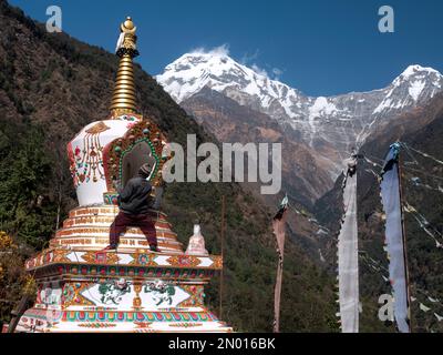 Chhomrong, Népal. Homme les derniers détails de la nouvelle stupa bouddhiste de village. Drapeaux et Annapurna Sud en arrière-plan. Banque D'Images