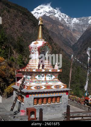 Chhomrong, Népal. Homme les derniers détails de la nouvelle stupa bouddhiste de village. Annapurna Sud en arrière-plan. Banque D'Images