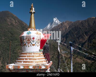 Chhomrong, Népal. Homme finissant les derniers détails de la nouvelle stupa de village. Mt Fishtail Machapuchare en arrière-plan. Banque D'Images